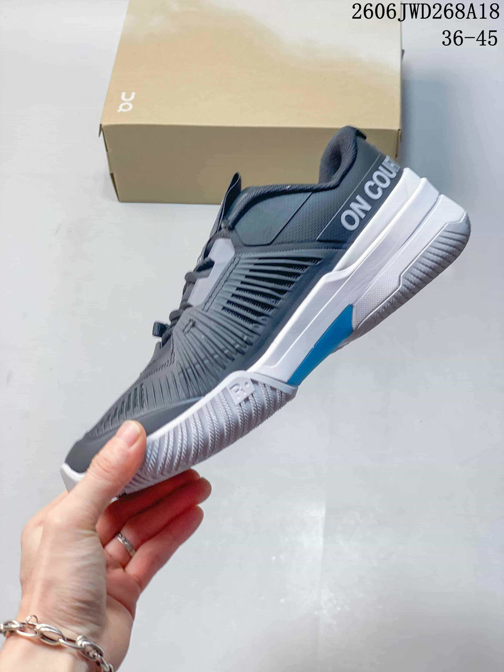 Side view of a gray tennis shoe with white and blue midsole accents.