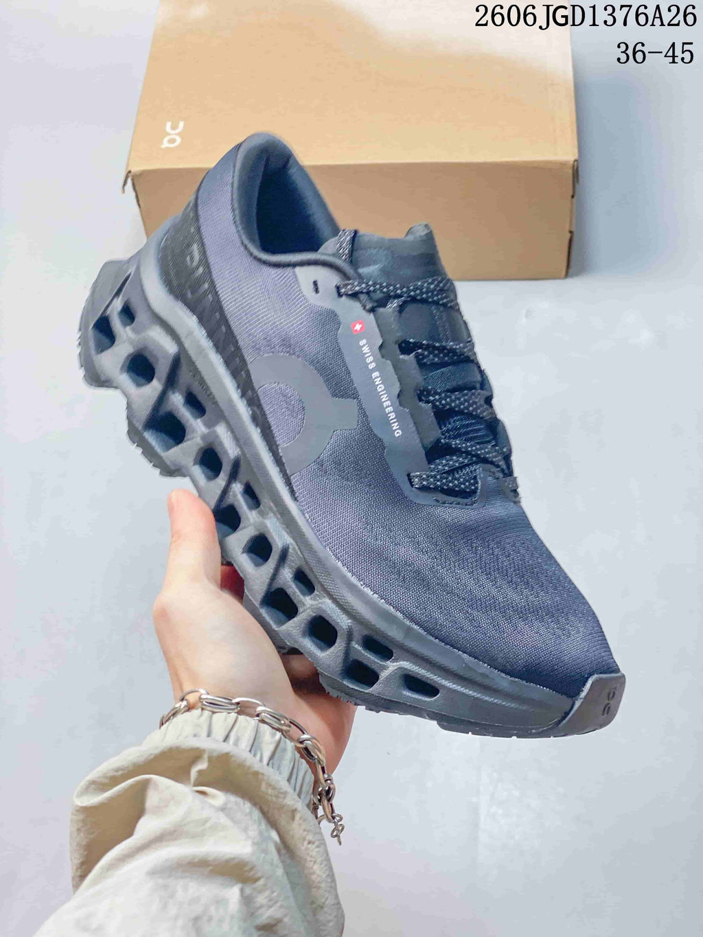 Side view of a slate On Cloudmonster 3 shoe with a sculpted open-channel midsole.