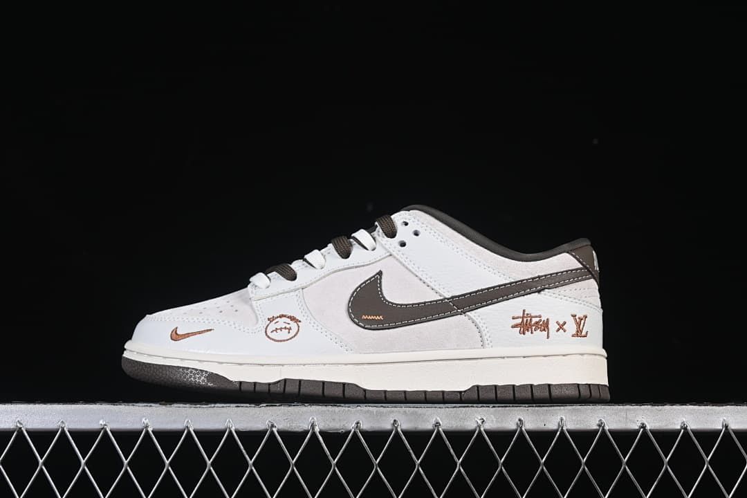 Side view of a white and light gray low-top sneaker with dark brown accents and decorative side graphics.