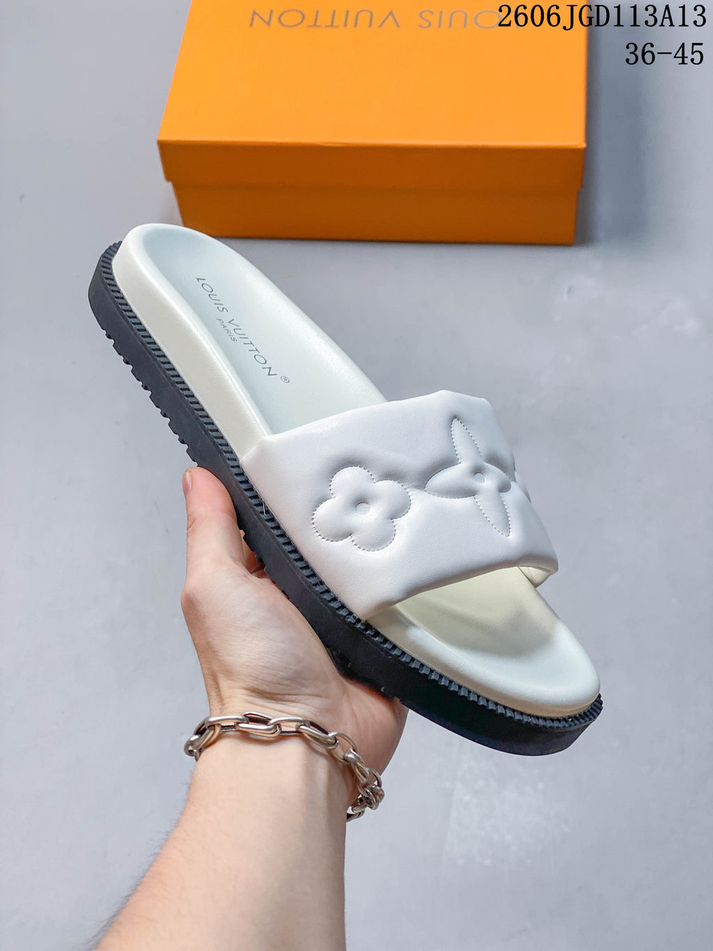 Close-up of a white slide sandal showing its wide floral-motif strap and dark ridged outsole.