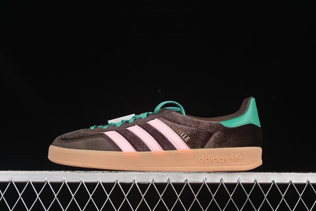 Side view of a single dark brown Gazelle Indoor sneaker with pink stripes and teal accents.