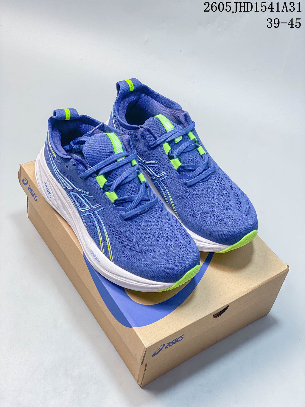 Pair of blue ASICS GEL-NIMBUS 26 running shoes with lime accents on a shoebox