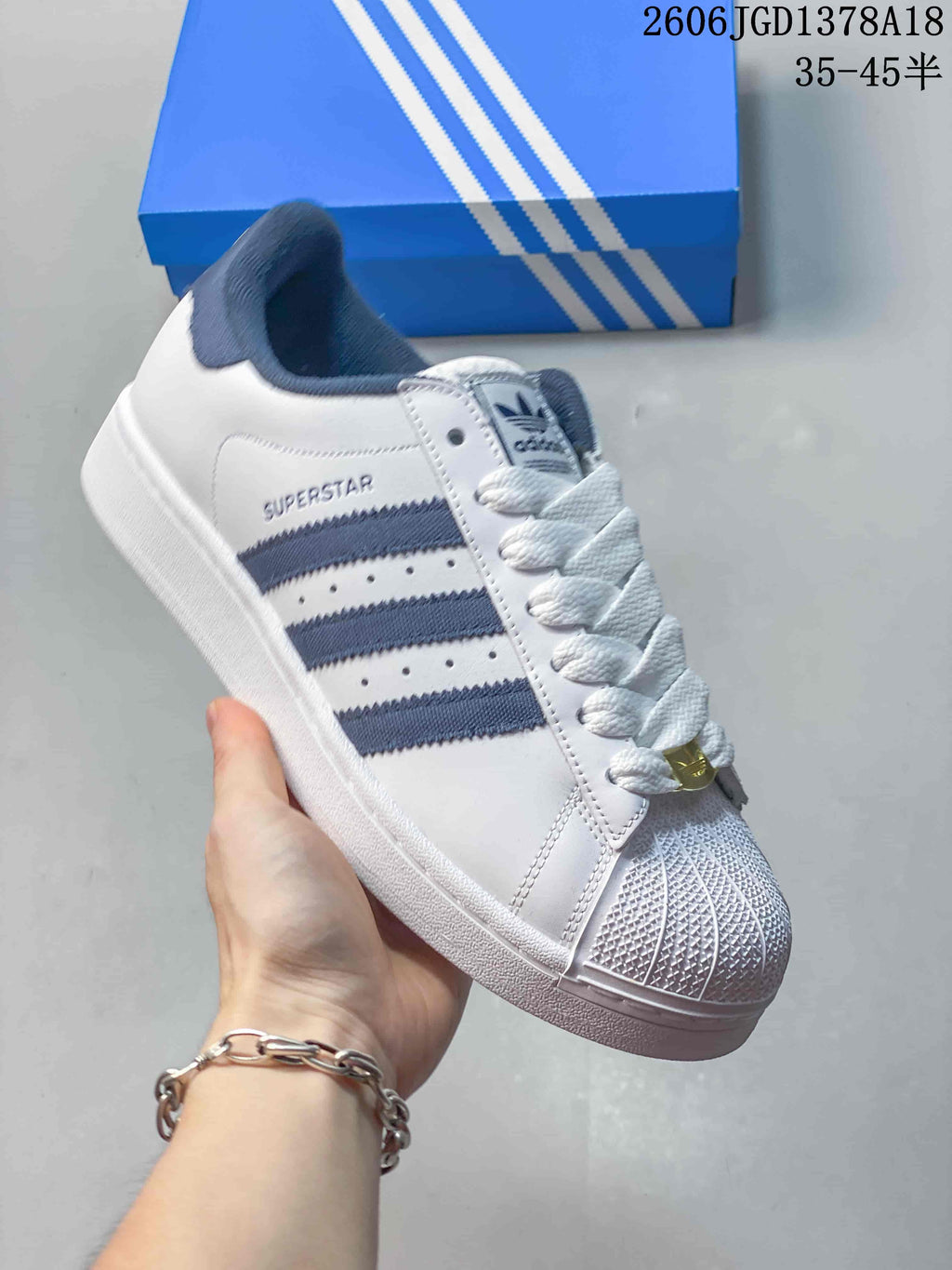 Angled view of a white Adidas Superstar sneaker with navy stripes and a shell-style toe.