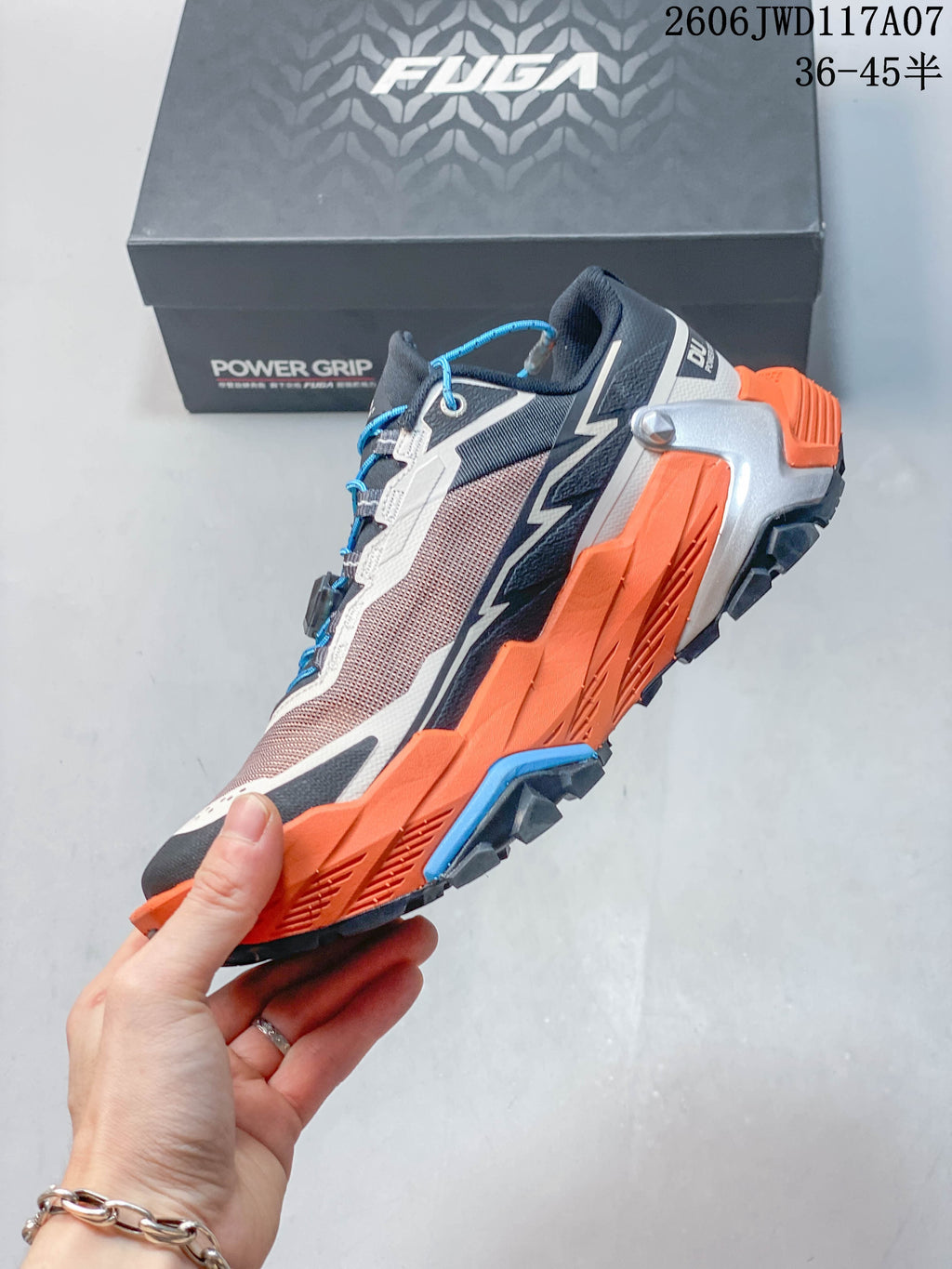 Side view of the Kailas trail shoe with orange midsole, grey panels and blue accents.