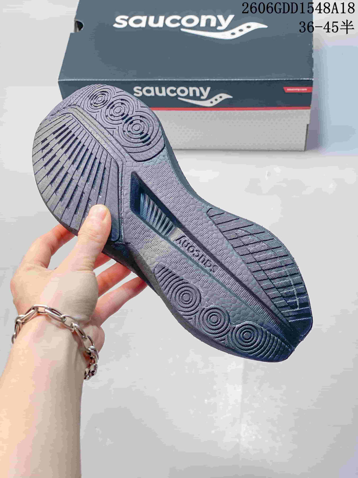 Underside of a Saucony running shoe showing patterned tread and the shoebox