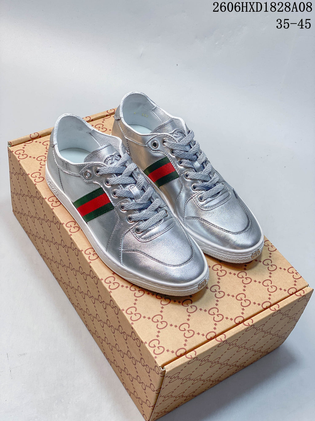 Pair of silver low-top lace-up sneakers with green-and-red side stripes and white soles, shown on a patterned box.