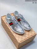 Pair of silver low-top lace-up sneakers with green-and-red side stripes and white soles, shown on a patterned box.