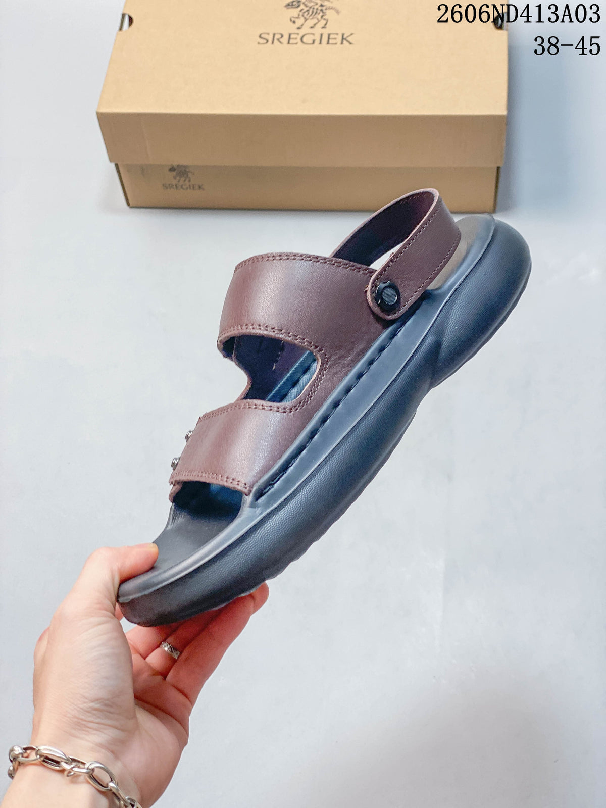Side view of a brown sandal with an adjustable heel strap and dark gray sole.