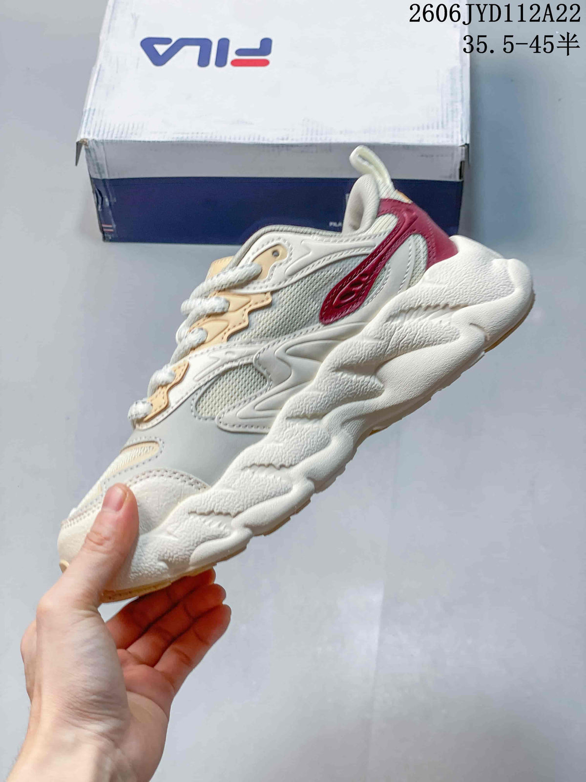Side profile of the cream FILA sneaker with beige panels, burgundy accents and a sculpted sole.