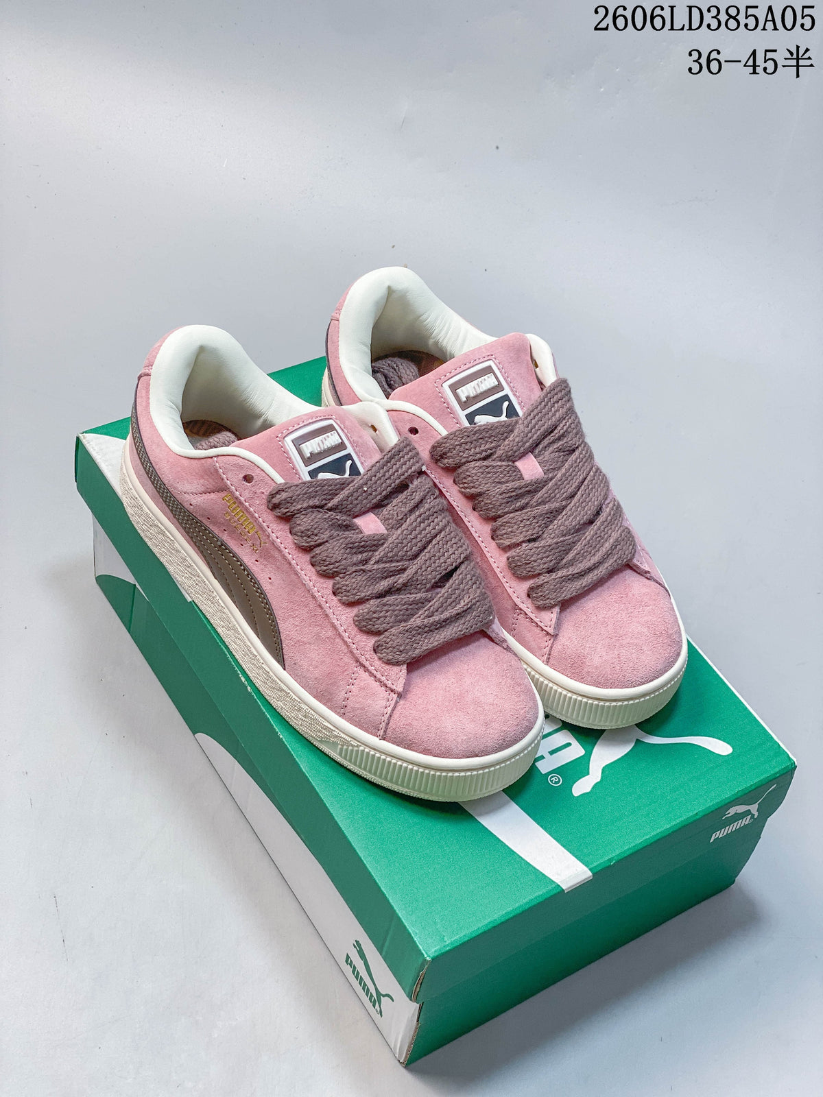 Pair of pink PUMA Suede XL-style sneakers with wide laces and contrasting side stripes, shown on a green shoe box