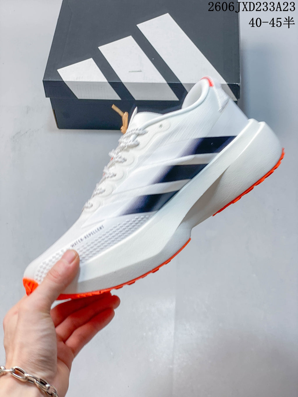 Side view of a white low-top running shoe with dark stripes and orange outsole accents