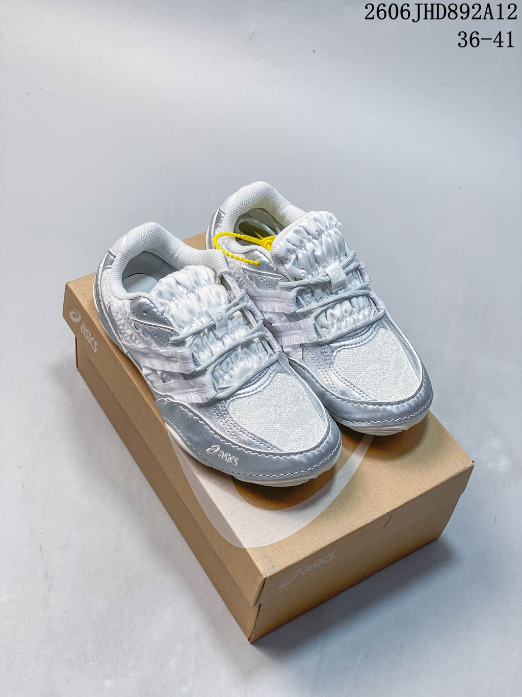 Pair of silver and light gray ASICS Hypersync sneakers shown on a shoebox