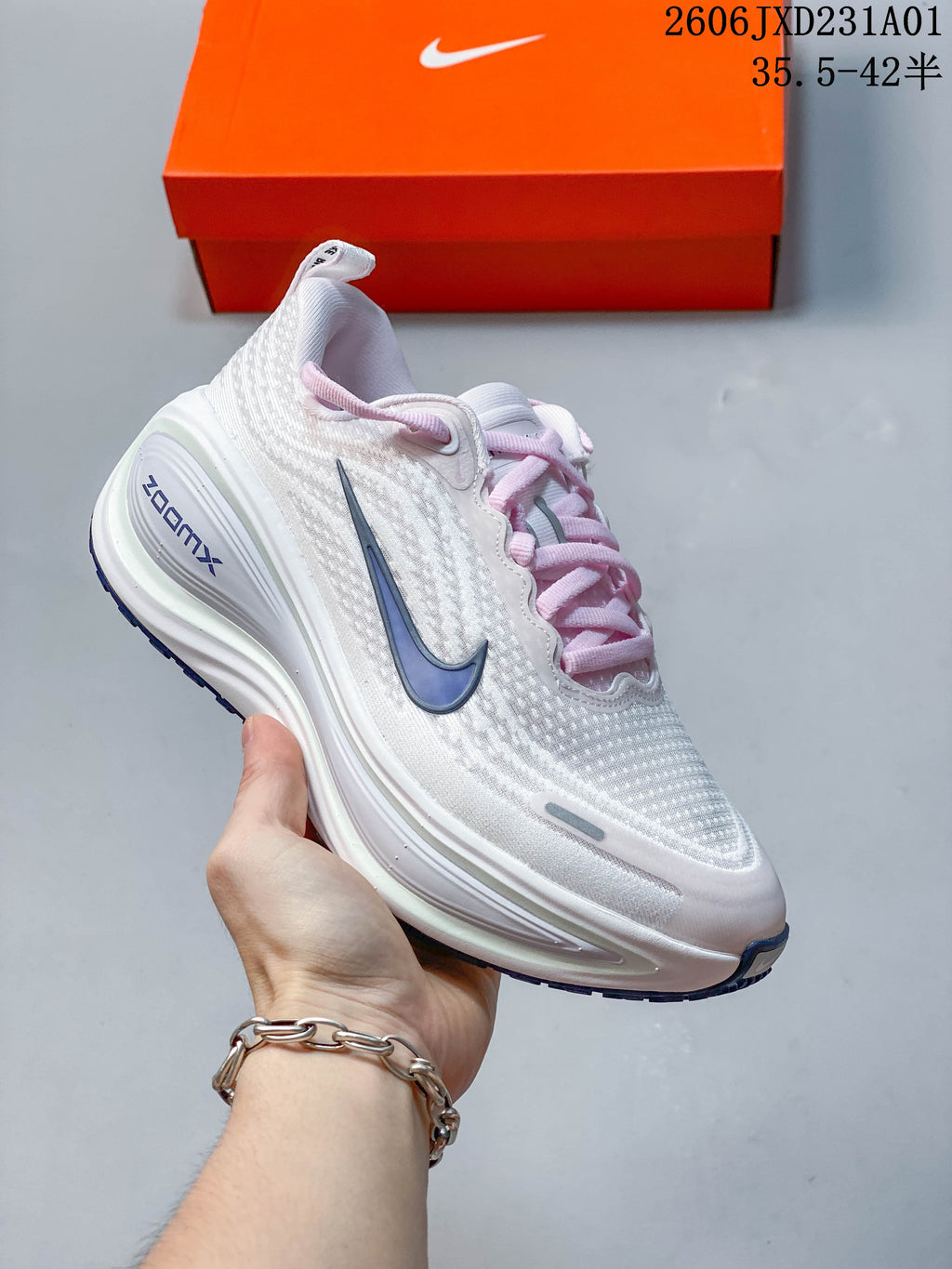 Side view of a white Nike Vomero Plus shoe with pale pink laces and blue-gray accents.
