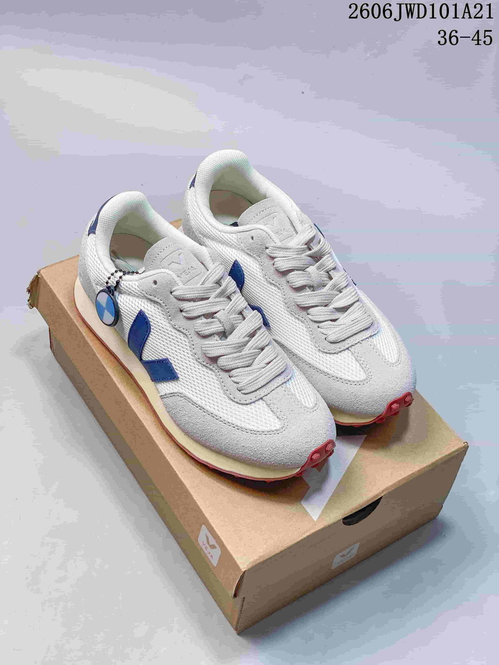 Pair of white and light gray Veja sneakers with blue side logos, shown on a shoe box