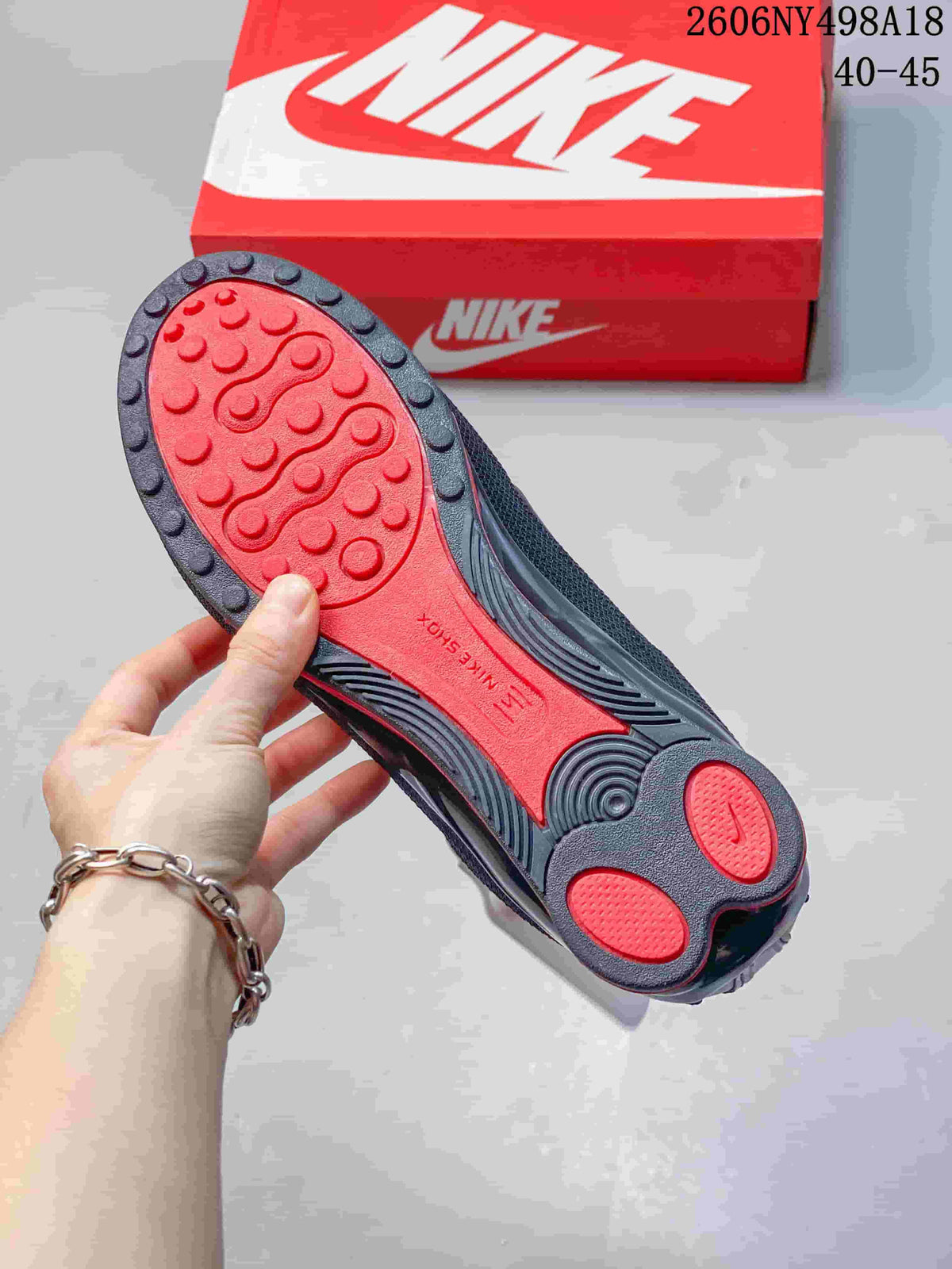 Underside of a Nike Shox TL sneaker showing a red and charcoal patterned outsole.