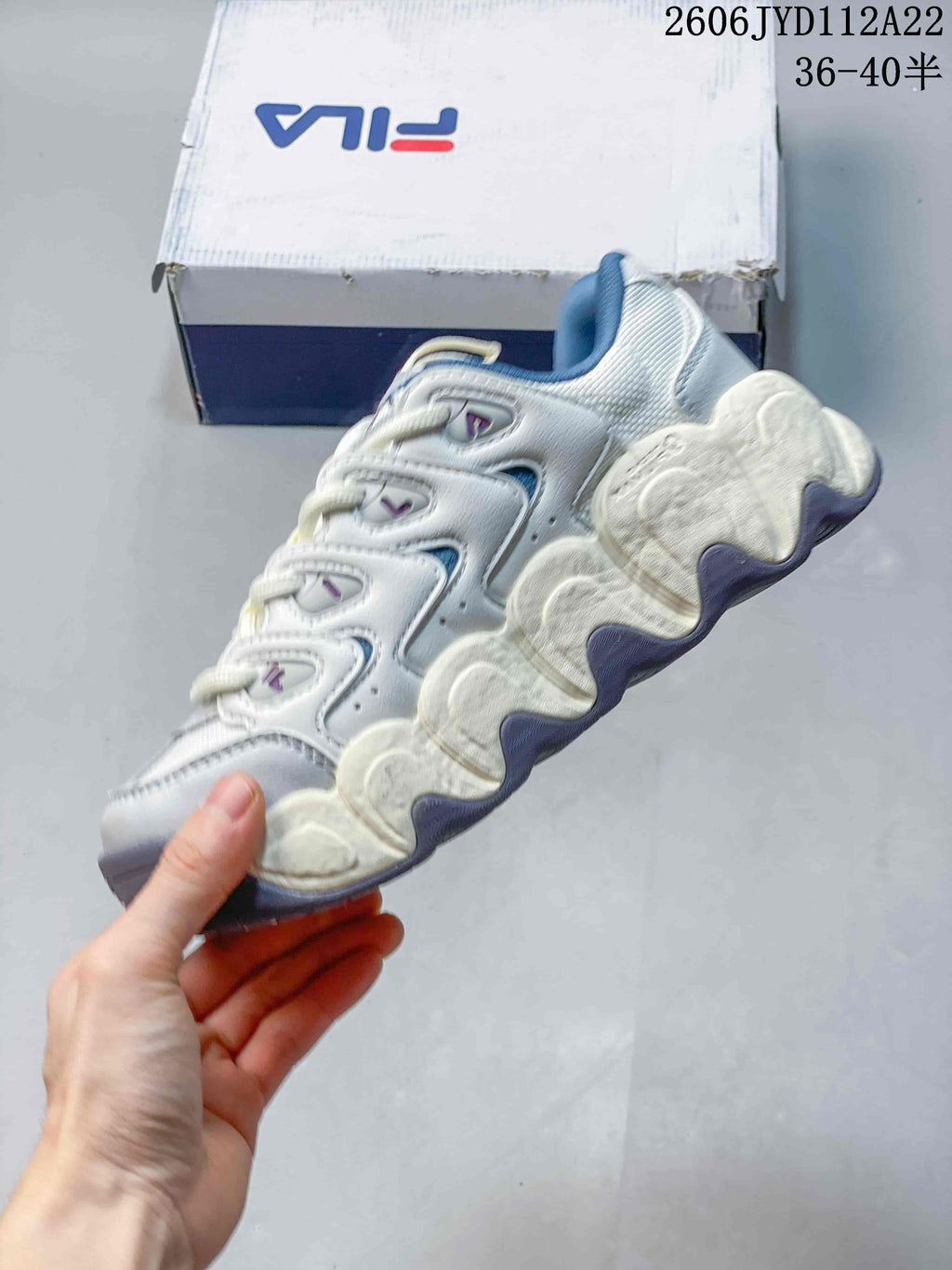 Side profile of a white and blue FILA sneaker with layered panels and a sculpted sole