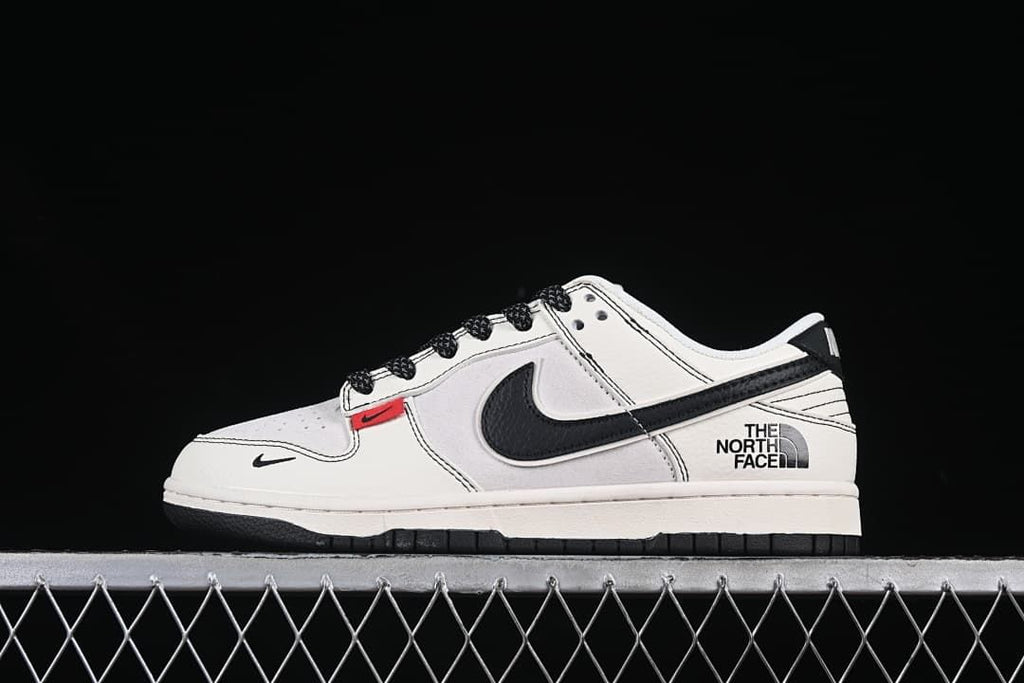 Side view of an off-white and black Nike SB Dunk Low with The North Face branding and a small red accent