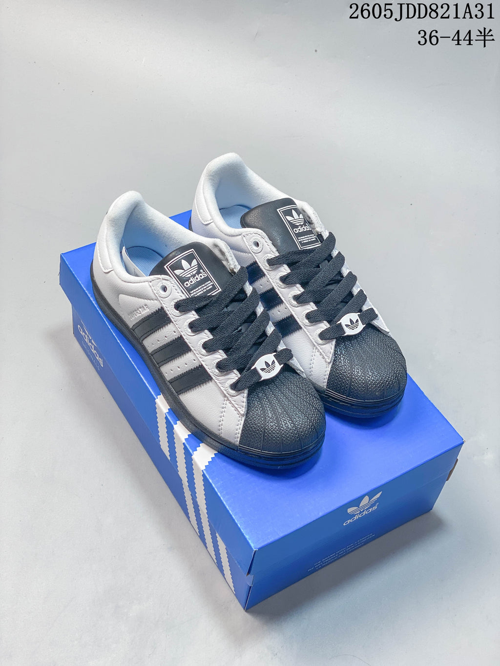 Pair of light-colored Adidas Superstar sneakers with dark shell toes, dark laces and three stripes.