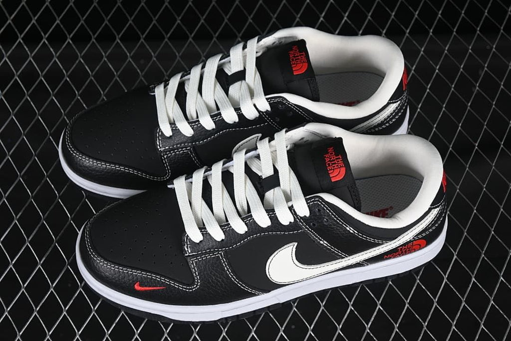 Pair of black low-top sneakers shown from above, with white laces, white Swooshes, and red accent graphics.