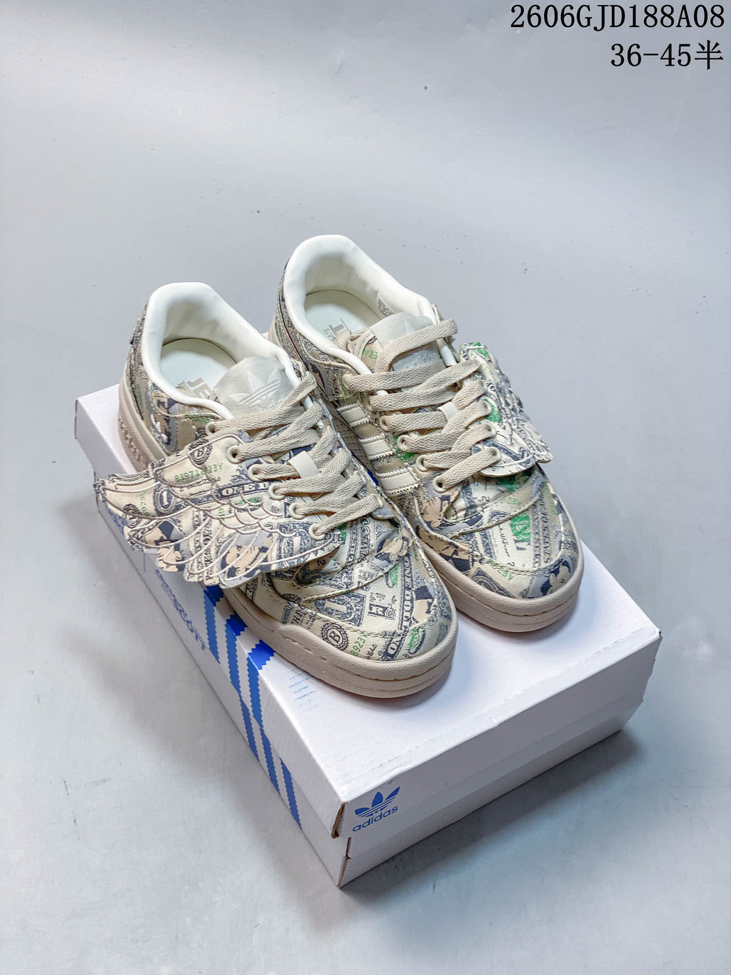 Pair of pale green and cream adidas Forum Low sneakers with banknote print and wing-shaped side details, shown on a shoebox