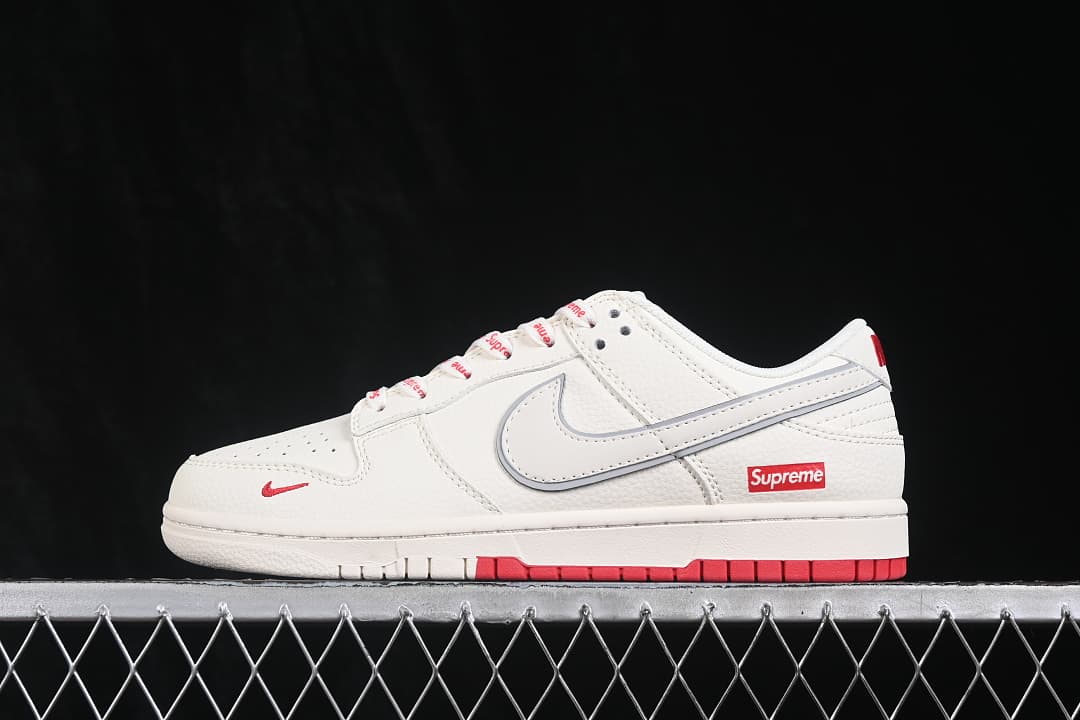 Side view of a white low-top sneaker with red accents, an outlined Swoosh, and a Supreme-branded heel detail.