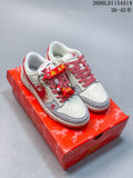 Pair of off-white and red Nike SB Dunk Low sneakers with decorative charms, displayed on a red patterned box.