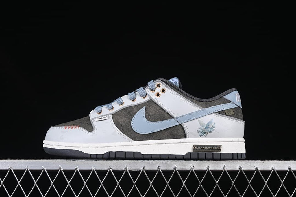 Side view of a gray, white, and pale blue Nike SB Dunk Low sneaker with a pigeon graphic on the heel