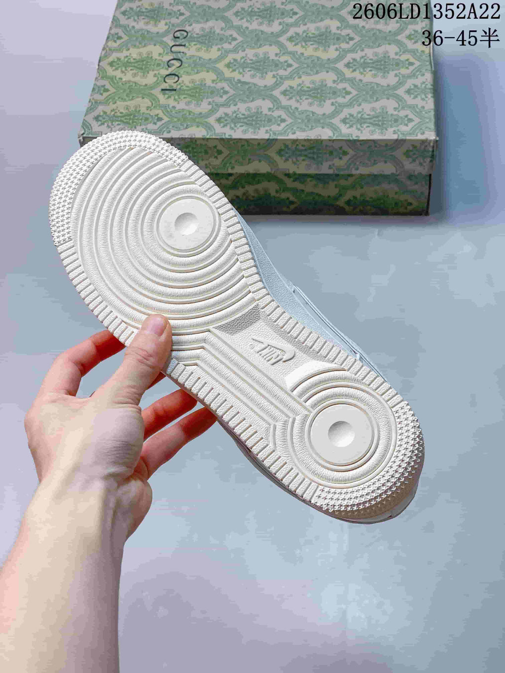 Close-up of the white sneaker outsole showing circular tread details; patterned box in the background.