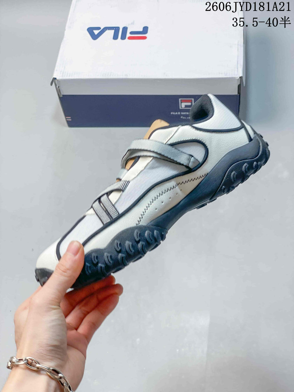 Side view of a white and gray FILA shoe with crossing straps and a dark outsole.