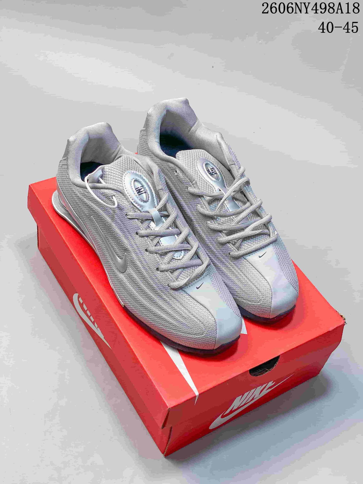 Pair of silver Nike Shox TL sneakers displayed on a red box