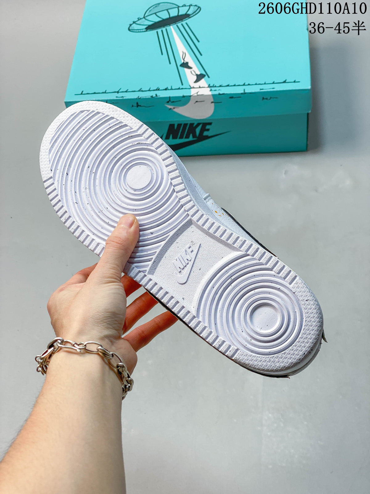 Underside of a white sneaker showing a circular-patterned outsole, with a turquoise shoe box in the background.