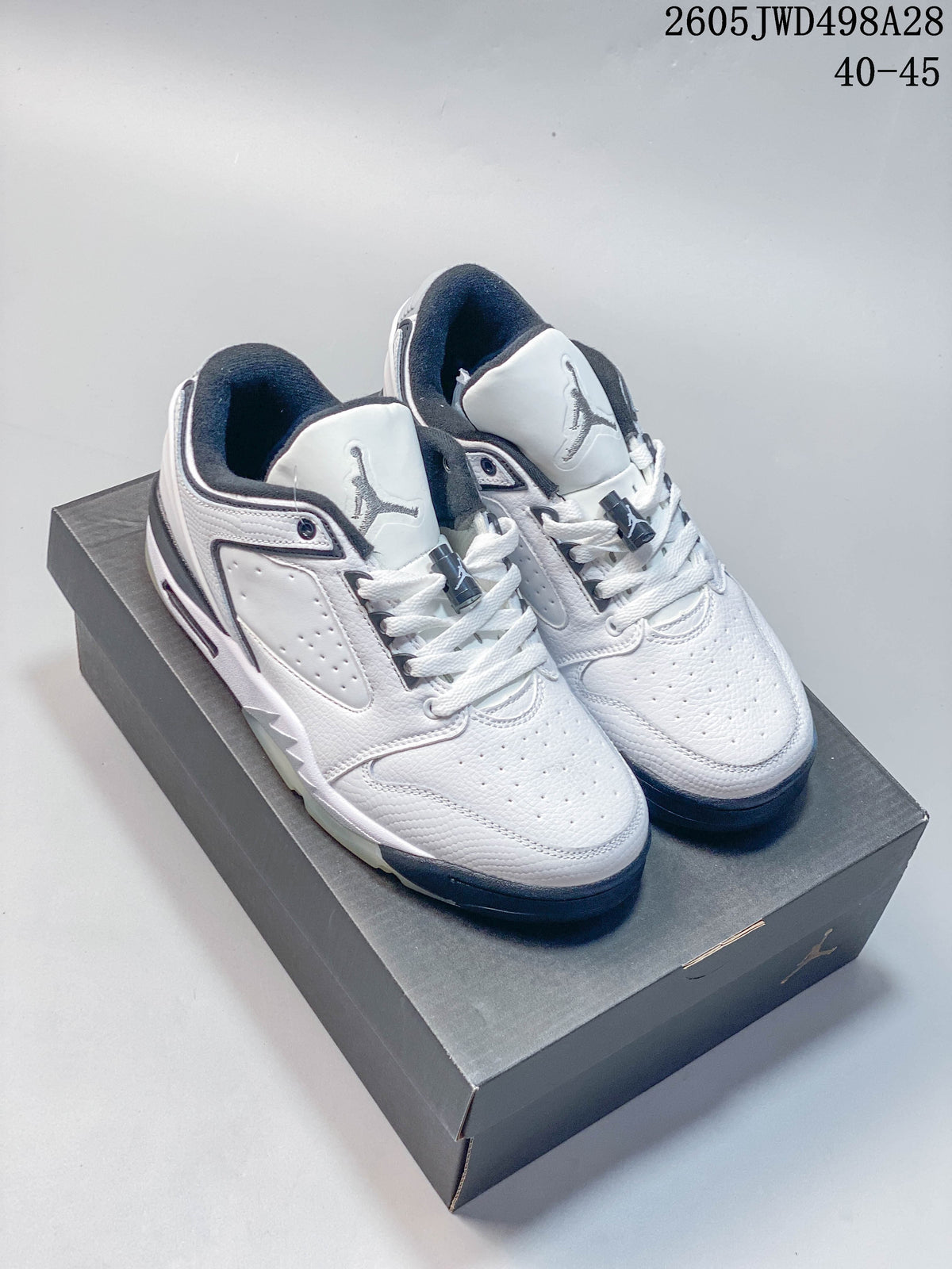 Pair of white low-cut Jordan sneakers with gray and dark navy details, shown on a shoebox.