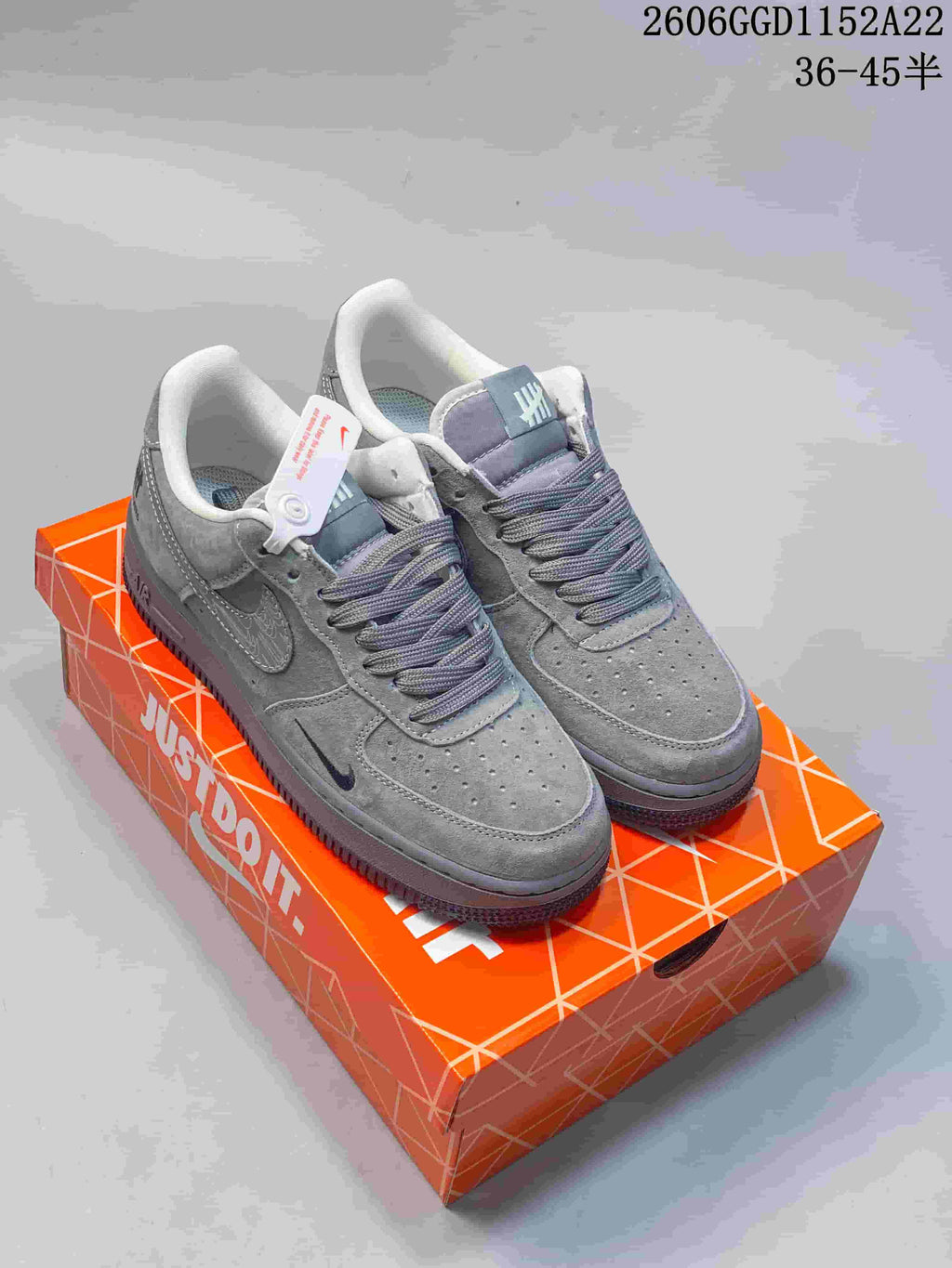 Pair of grey Nike Air Force 1 low-top sneakers with patterned Swooshes on an orange shoebox