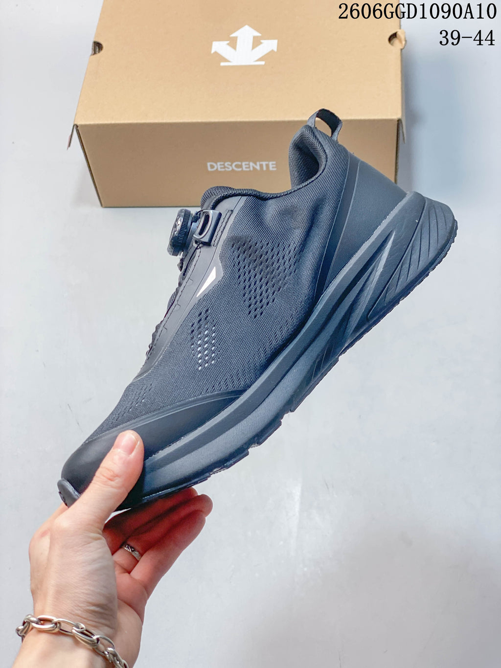 Side profile of a dark gray Descente sneaker showing perforated upper panels and dial closure; image text lists sizes 39–44.