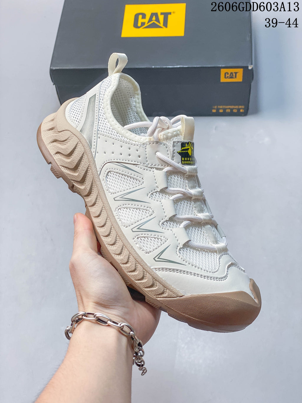Angled side view of a white and beige CAT sneaker with layered overlays