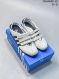 Pair of white and gray Adidas Samba-style low-top sneakers with three straps, shown on a blue shoe box.