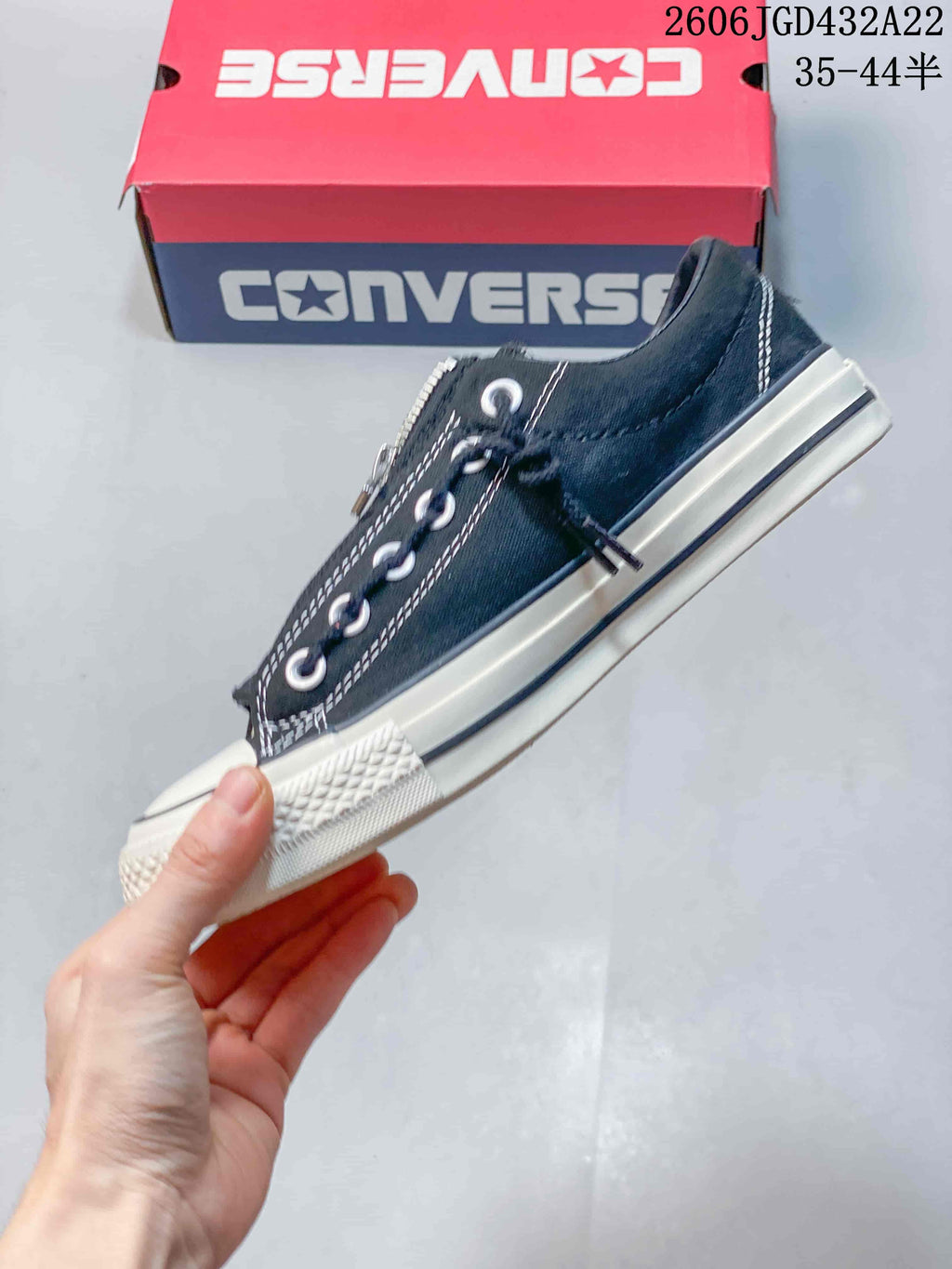Side view of a black Converse low-top sneaker with zipper, laces, and off-white sole.