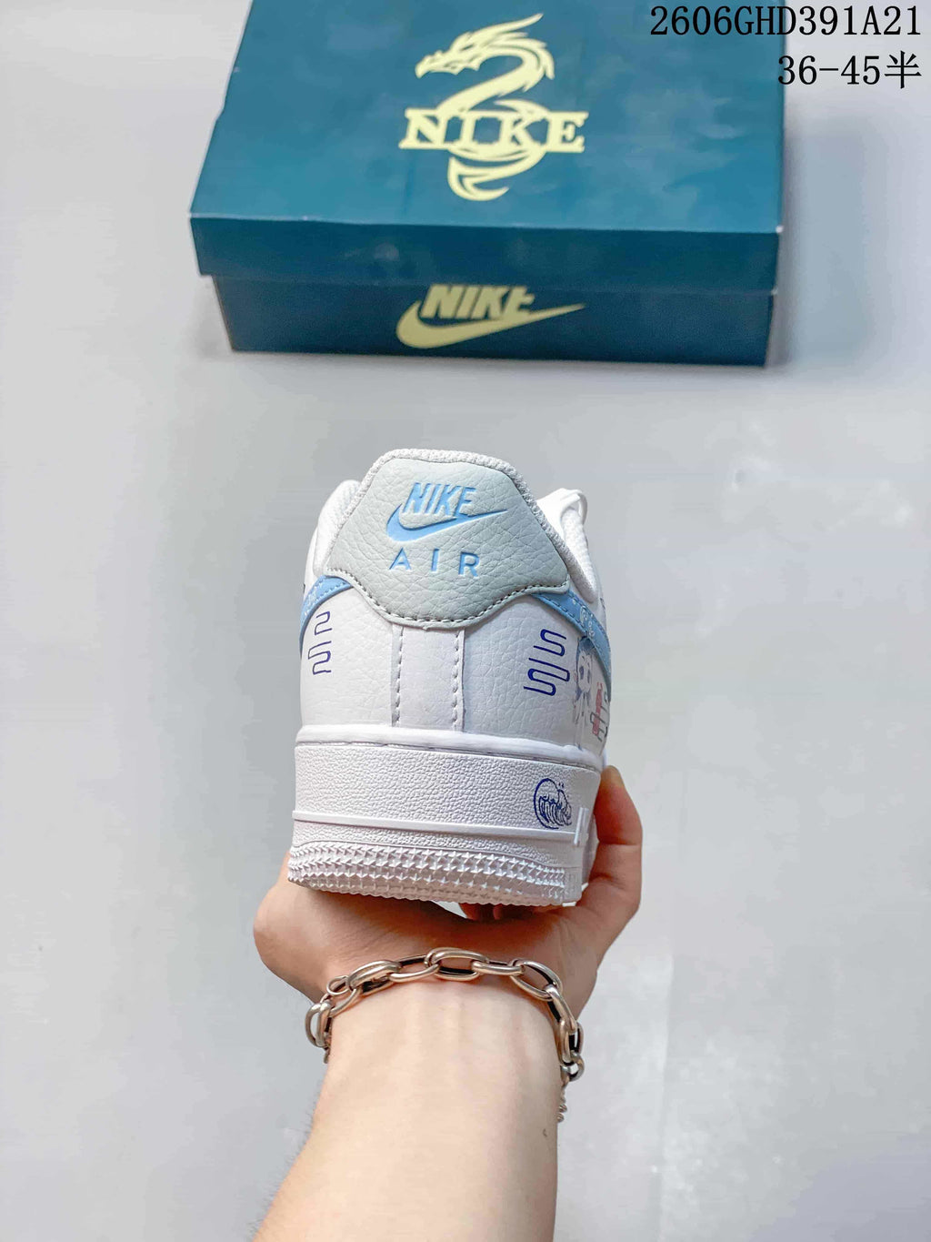 Rear view of the white sneaker with light-blue heel detailing and decorative graphics.