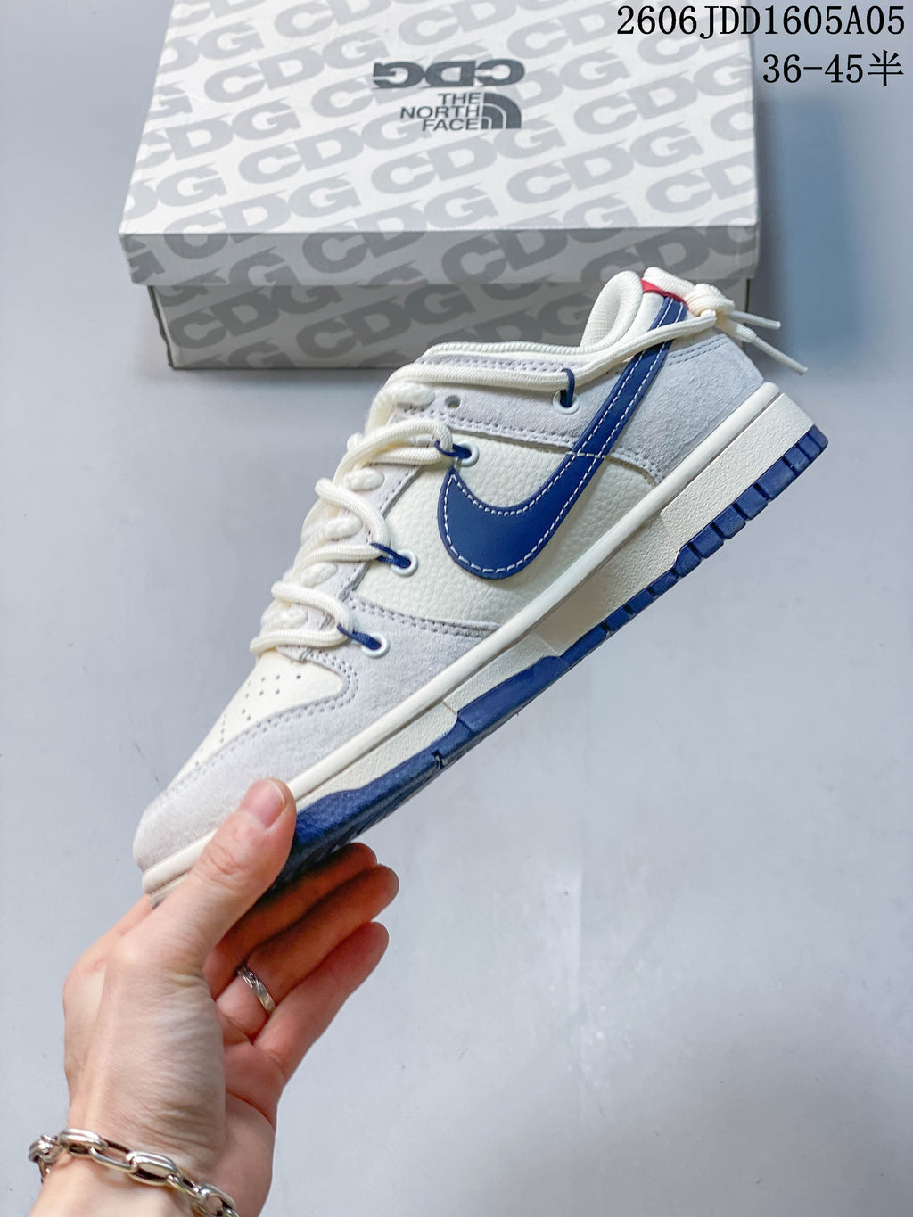 Side view of an off-white Nike SB Dunk Low with a navy Swoosh and layered panels.