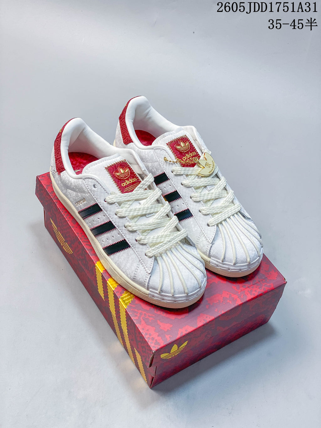 Pair of white Adidas Superstar sneakers with dark stripes, red accents, and shell toes