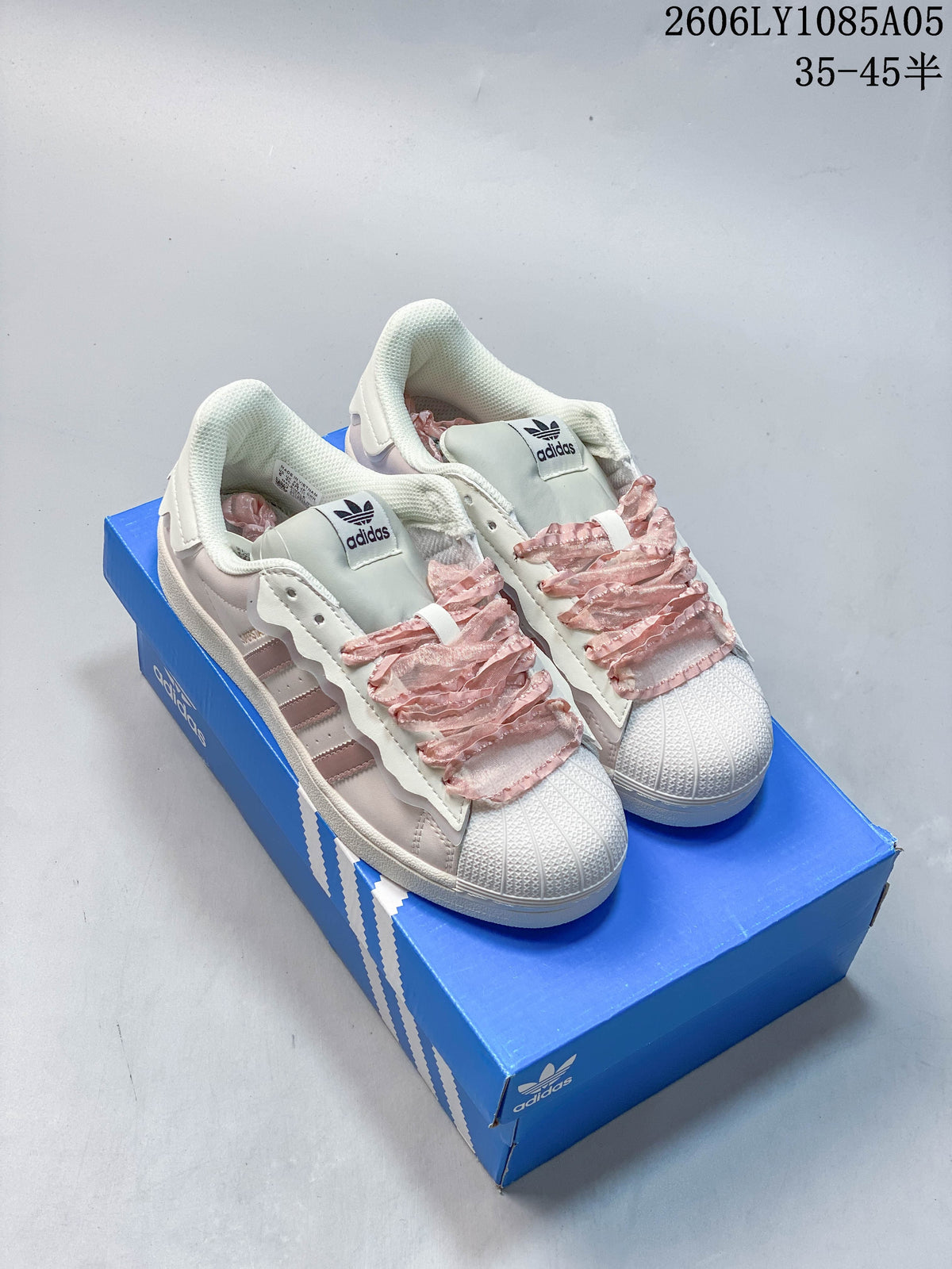 Cream and blush pink Adidas Superstar sneakers with decorative ruffled laces on a blue shoe box