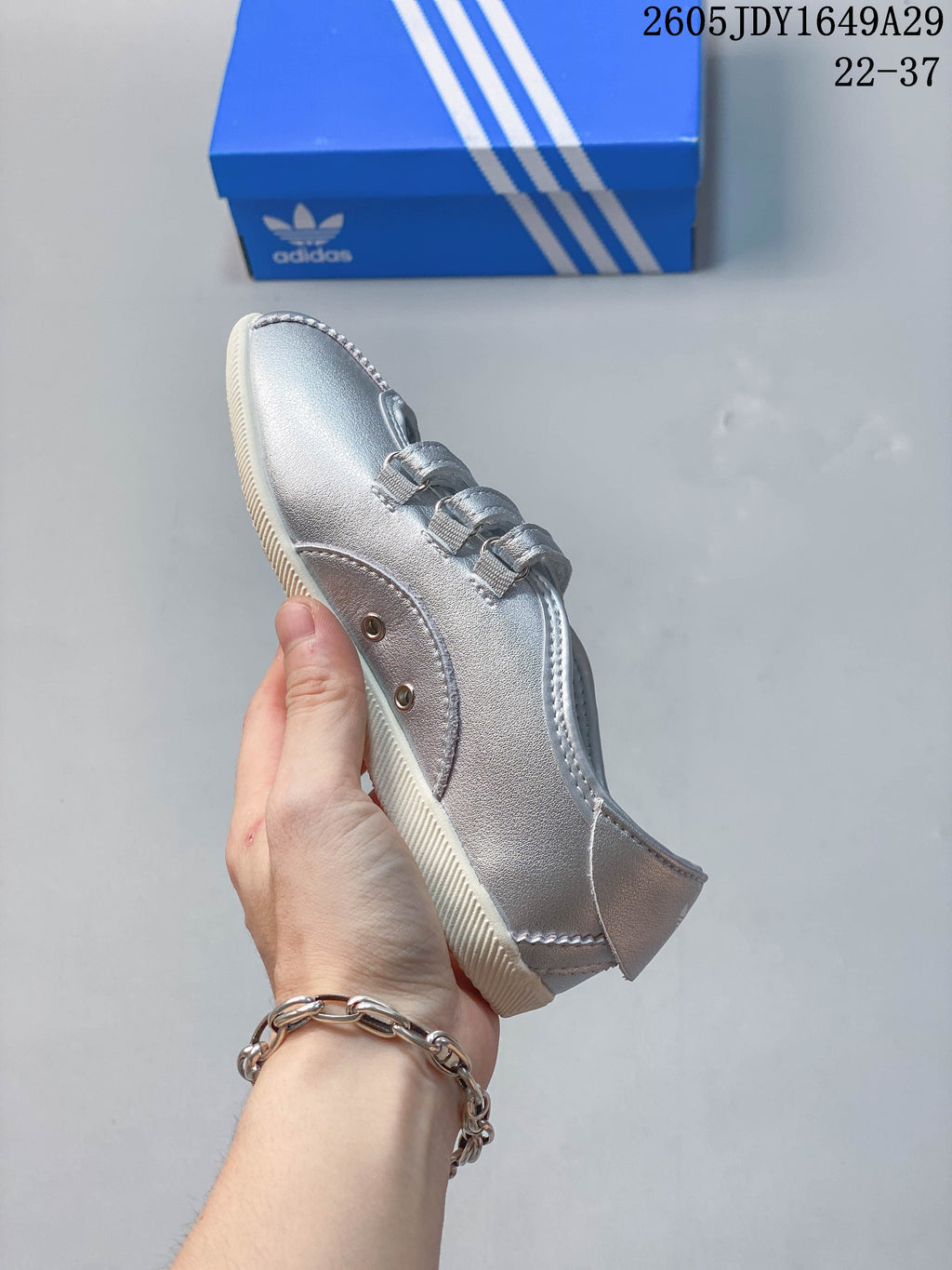 Side profile of a silver sneaker with three straps and stitched panels