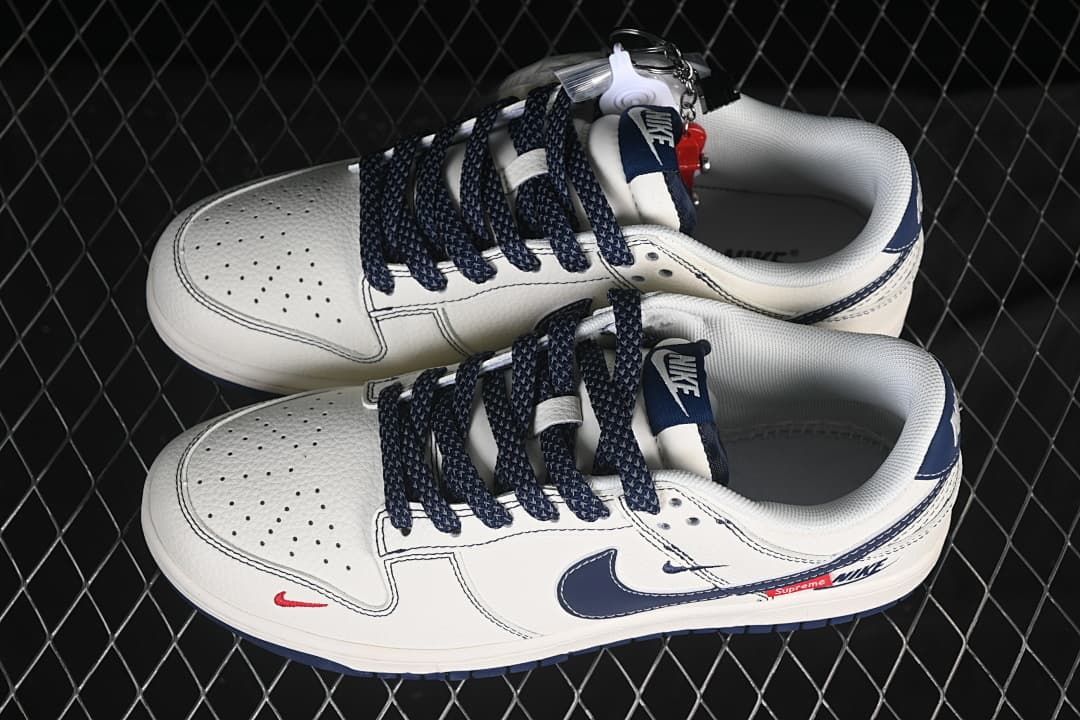Top view of a pair of white and navy low-top sneakers with dark laces and red details